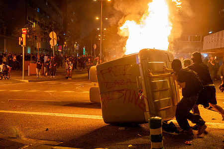 Protesters push a burning container during the riots in front of the Israeli consulate. A demonstration linked to the general strike in support of Palestine ended in violent clashes outside the Israeli consulate. Protesters burned containers and threw stones, prompting police to respond with force, using heavy charges and pepper spray to disperse the crowd.