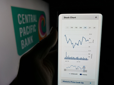 In this photo illustration, a person is holding a smartphone with the web page of financial company Central Pacific Bank (CPB) on screen in front of logo.
