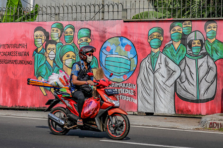 A motorist rides past a mural appreciating doctors and medical personnel for fighting COVID-19, in Jakarta.Indonesian Government officially implements "large scale social restrictions" in Jakarta amid the COVID-19 coronavirus pandemic, which city authorities ban any gathering of more than five people and includes transportation restrictions, began April 10 for 14 days. At least 24 Indonesian medical personnel have died from coronavirus exposure after treating patients who were positive for COVID-19, according to the Indonesian doctor's organization.