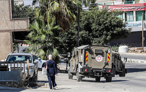 A Palestinian woman walks near Israeli military vehicle during a raid to arrest Palestinians in the city of Nablus.