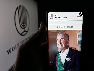 In this photo illustration, a person is holding a smartphone with the webpage of Israeli organisation The Wolf Foundation on screen in front of logo.
