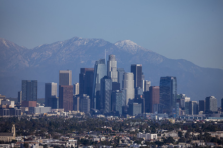The San Gabriel Mountains rise behind the downtown Los Angeles skyline on Monday, Dec. 29, 2025. Rain is forecast for the 2026 Rose Parade on New Year’s Day in Pasadena, with an 80–90% chance of showers—potentially marking the first wet parade in 20 years—as organizers prepare floats for moisture and advise spectators to bring ponchos.