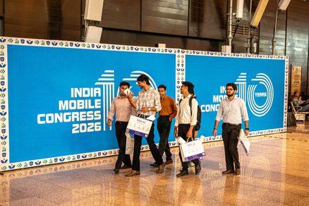 Visitors, mostly college students, pass by a poster of India Mobile Congress 2026 during its 10th edition at Yashobhoomi India International Convention and Expo Centre. India Mobile Congress (IMC) 2026 is a major technology and telecommunications event held in India, bringing together telecom companies, technology companies, startups, government officials, investors, researchers and innovators. The event is jointly organised by the Department of Telecommunications (DoT) and the Cellular Operators Association of India (COAI).