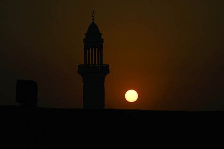The sun sets behind the silhouette of a mosque minaret in Doha.
