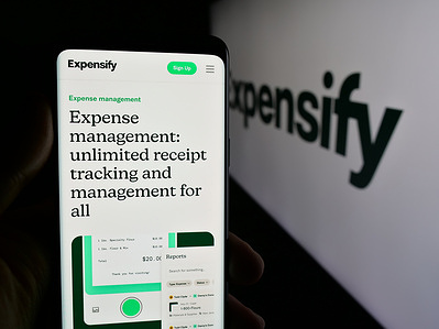 In this photo illustration, a person is holding a cellphone with the webpage of expense management company Expensify Inc. on screen in front of logo.