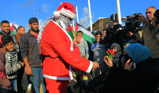 A Palestinian seen wearing Santa Clause clothes distributing flowers to people on the eastern border of Khan Younis during the Christmas festive season.