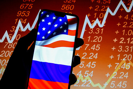 In this photo illustration, the United States and Russian flags seen displayed on a smartphone with stock market prices in the background.