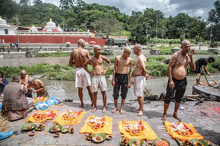 A Hindu priest guides bereaved relatives as they perform symbolic rituals using 'Kush' grass effigies on the banks of the Bagmati River at Pashupatinath Temple in Kathmandu, Nepal. Following devastating flash floods across Nepal that left many dead and missing, families conducted mass Hindu cremation rites. The ceremonies combined actual cremations for recovered bodies with symbolic rites using 'Kush' grass effigies to liberate the souls of those still unaccounted for.