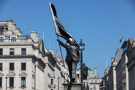 A statue attributed to Banksy in Waterloo Place in central London. The work depicts a lone figure stepping down from a plinth, its face obscured by a billowing flag, in a style characteristic of the artist's politically charged interventions. The installation, bearing Banksy's name at the base positioned near the Athenaeum Club and the Crimean War Memorial, the piece contrasts with the area's traditional monuments and historic architecture.