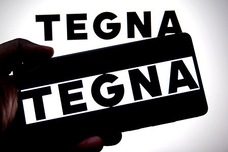 In this photo illustration, a Tegna logo is seen displayed on a smartphone and in the background.