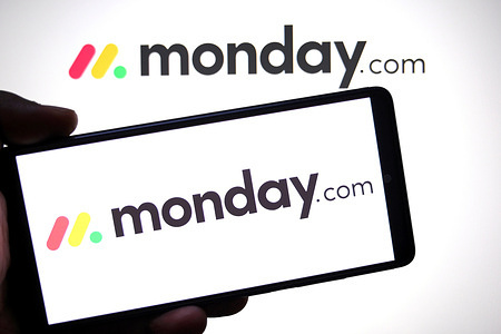 In this photo illustration, the Monday.com logo is seen displayed on a smartphone and in the background.
