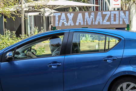 SEATTLE, UNITED STATES - MAY 01, 2020: A vehicle with a placard saying, 'tax Amazon' during the demonstration.
A caravan of autos and bicyclists encircle Amazon headquarters demonstrating in support of city council member, Kshama Sawant's proposal to impose new taxes on Amazon and other large businesses, to fund COVID-19 relief and other programs.