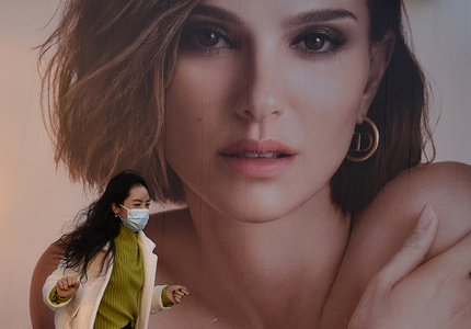 A woman wearing a face mask as a precaution against the spread of coronavirus, walks past a billboard of Christian Dior in Sanlitun District.