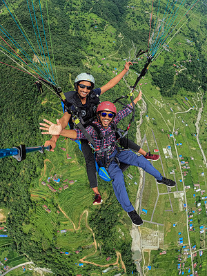 A tourist enjoys paragliding with a paragliding pilot over Pokhara and Phewa Lake.