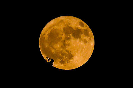The full flower moon drifts passing in front of a construction crane.