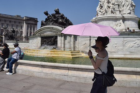 People shelter under an umbrella from the scorching sun next to the Victoria Memorial outside Buckingham Palace as extreme heat hits UK and Europe.