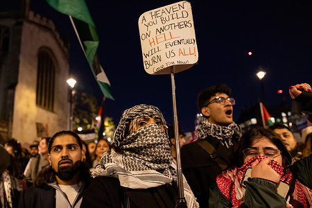 A protester holds a sign while demonstrating outside the UK Parliament at Westminster. Pro-Palestine supporters gather outside Parliament Square this evening as the Members of Parliament are voting on the amendment of ceasefire from the King's speech proposed by the Scottish National Party (SNP). They demand an immediate ceasefire and to stop the aerial bombardment and innocent killings of Palestinians trapped in Gaza by Israeli forces.