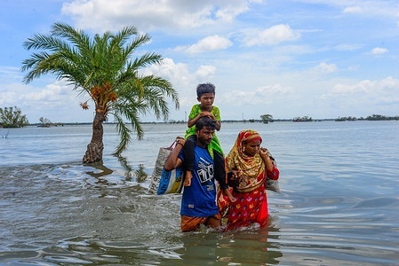 People are seen crossing a flooded road as the embankment of the coastal area was broken after the landfall of cyclone Amphan.Thousands of shrimp enclosures have been washed away, while numerous thatched house, trees, electricity and telephone poles, dykes and croplands were damaged and many villages were submerged by the tidal surge of the Amphan in Satkhira District.