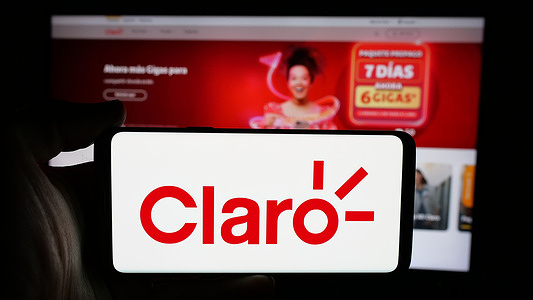 In this photo illustration, a cellphone with the logo of telecommunications company Claro Ecuado on screen in front of webpage.