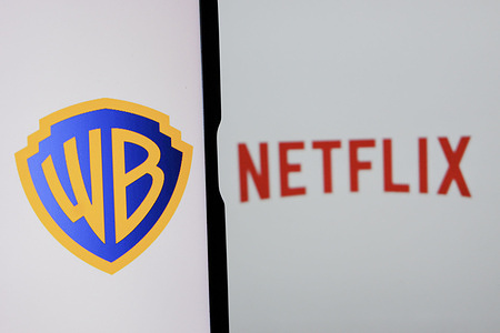 In this photo illustration, the Warner Bros logo is displayed on a mobile phone screen with a Netflix logo in the background..
