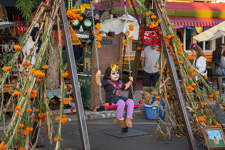 A child wearing calavera face paint rides a swing decorated with marigold flowers during the Día de los Muertos (Day of the Dead) festivities. Thousands gathered in San Diego’s Barrio Logan Cultural District to honor the Día de los Muertos (Day of the Dead), a Mexican tradition that celebrates the lives of departed loved ones. The event featured colorful altars, live music, and street food.