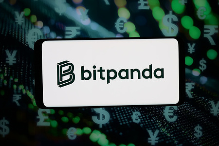 In this photo illustration, the logo of Austrian crypto trading company Bitpanda GmbH is displayed on a smartphone in front of abstract background on computer screen.