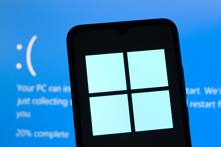 In this photo illustration, the Microsoft Windows logo is seen displayed on a smartphone screen with a blue screen in the background.