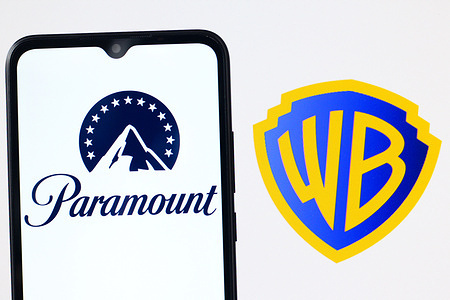 In this photo illustration, the Paramount logo is seen displayed on a smartphone screen and the Warner Bros Discovery logo in the background