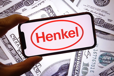 In this photo illustration, the Henkel company logo is seen displayed on a smartphone screen with United States dollar banknotes in the background.