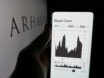 In this photo illustration, a person holds a smartphone with the webpage of US home furnishings company Arhaus Inc. on screen in front of a logo.