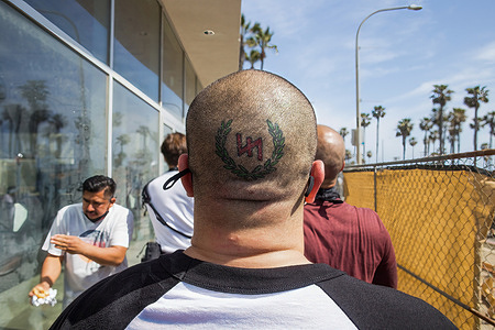 A man with a tattoo on the back of his head related to neo-Nazi groups walks away from the protesting crowd after partaking in a physical altercation with counter-protesters.Upon word spreading amongst various social media and messaging platforms that there was to be a "White Lives Matter" protest at the Huntington Beach Pier at 1pm, a large group of counter protesters arrived at the pier to stop the "White Lives Matter" protest. The day resulted to clashes between counter protesters and white lives matter protesters both verbal and physical.