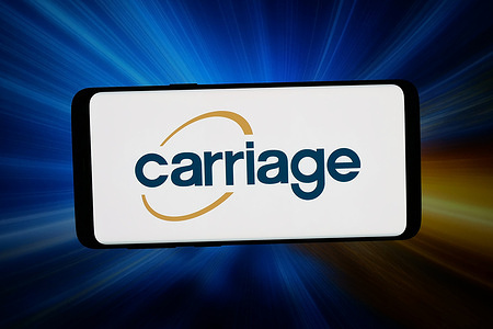In this photo illustration, the logo of US funeral company Carriage Services Inc. is displayed on a smartphone in front of abstract background on computer screen.