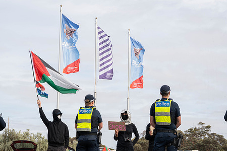 General view of protesters behind a police line, in front of the Avalon airshow flags. Pro Palestine Protesters attempted to disrupt the entry to the Avalon Airshow as they claim weapons being used in the ongoing war in Palestine are being put on display and they are being traded. The protesters got on the road once, but they were quickly outnumbered by police.