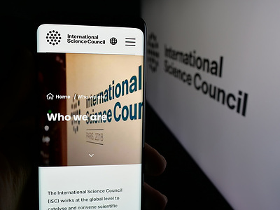 In this photo illustration, a person is holding a smartphone with the webpage of International Science Council (ISC) on screen in front of logo.