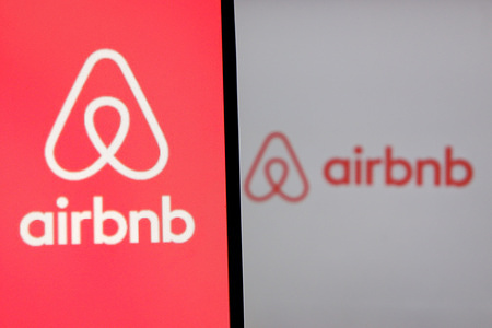 In this photo illustration, an Airbnb logo is displayed on a smartphone and in the background.