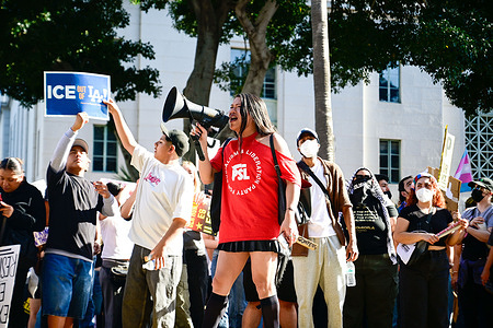 A woman shouts on a megaphone while thousands gather in front of the Los Angeles City Hall in response to recent ICE raids and arrests in the United States.