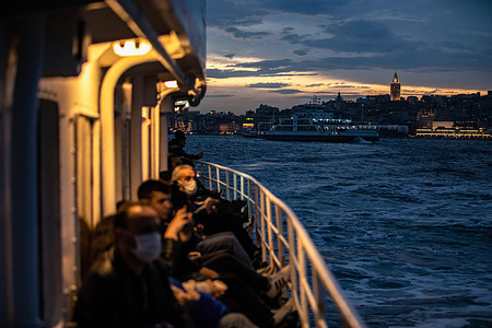 Passengers on the city lines ferry cruising towards Kadikoy with the Galata Tower in the background, during cloudy weather in the evening before the rain around Eminonu to Kadikoy.