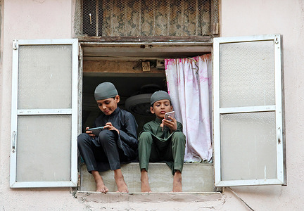 Muslim boys seen using mobile phones as they sit on the balcony of their house after performing Eid al-Fitr prayers marking the end of the holy fasting month of Ramadan at Brihanmumbai Municipal Corporation (BMC) ground, Mumbai. Eid-al-Fitr is celebrated by Muslims worldwide marking the end of month long fasting from dawn to dusk during the holy month of Ramadan.