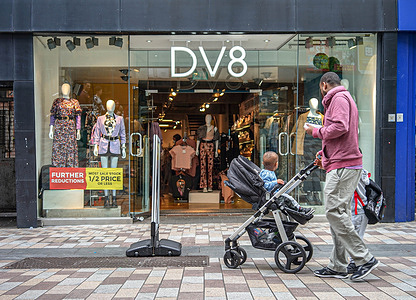 A man and his children pass by DV8 Fashion Store on Ann Street, Belfast.