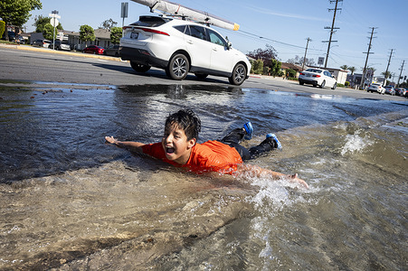 A boy plays in water from a broken fire hydrant in Rosemead, California, seeking relief as spring heat breaks temperature records across the Southland.