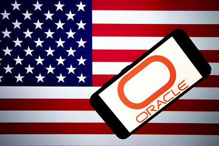 In this photo illustration, the Oracle logo is seen displayed on a mobile phone screen with American flag in the background.