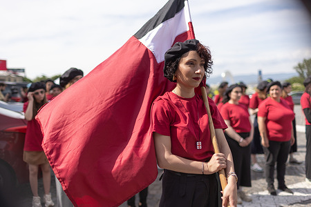 A young woman holds the Georgian national flag during the Shevardeni commemorative march. Young women march during Georgia’s Independence Day celebrations. Dressed in coordinated sports-style outfits, participants reenacted a historic 1919 photograph of female gymnasts from the “Shevardeni” society.