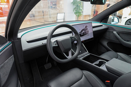 The interior of a Tesla Model Y showcasing the steering wheel, central touchscreen and ambient lighting seen displayed at Global Harbor.