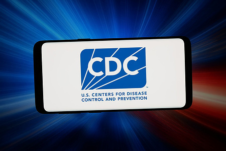 In this photo illustration, the US public health agency CDC logo is seen displayed on a smartphone in front of abstract background on computer screen.