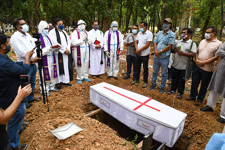 A bishop wearing a protective suite offering last prayers for a covid 19 deceased man during a burial by Bangladeshi Christians at a cemetery.