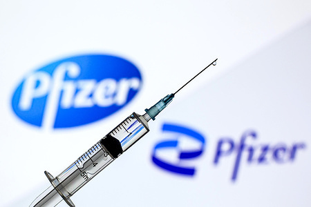 In this Photo illustration , a close up of a syringe in front of the Pfizer old logo and the Pfizer new logo.
