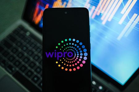 In this photo illustration, a Wipro logo is seen displayed on a smartphone with stock market graphics in the background.
