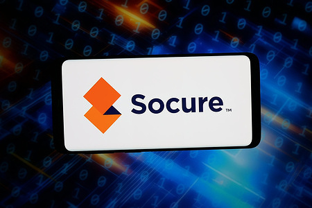 In this photo illustration, the US identity verification company Socure Inc. logo is seen displayed on a smartphone in front of abstract background on computer screen.