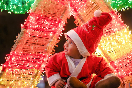 A girl dressed as Santa Claus poses for photos in front of the Christmas decorations during Christmas Eve at the Lalitpur shopping center.