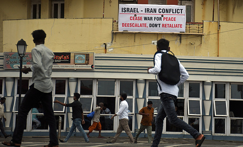 People walk past a poster with a message urging Israel and Iran to cease war for peace, "de escalate don't retaliate" is seen hunging above a restaurant wall in Mumbai. Conflict broke out between Israel and Iran on 13th June 2025 where Israel attacked Iran's key military and nuclear facility. Israel launched operation Rising Lion to roll back Iran's threat to Israel's survival.